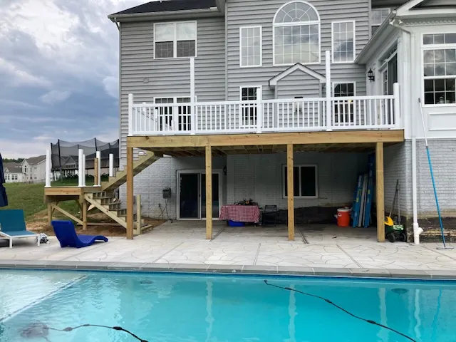 Elevated deck with white railings over a pool patio