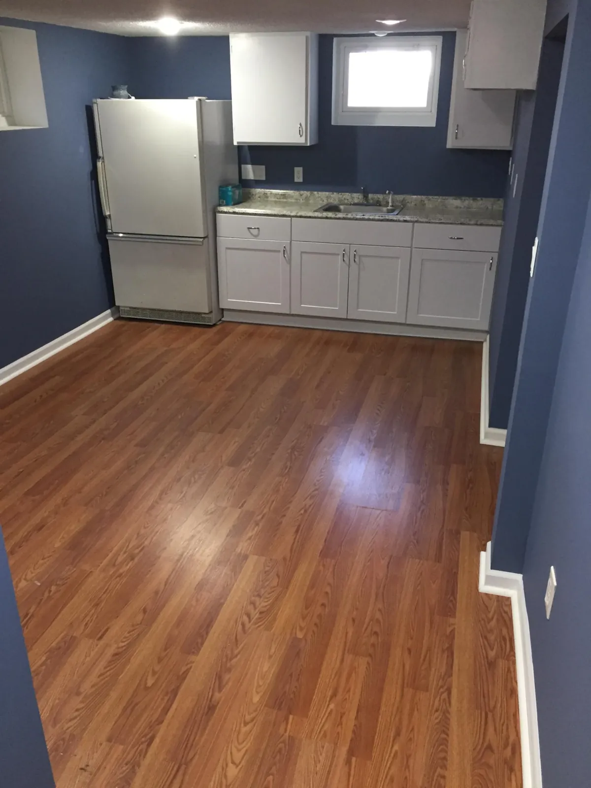 Finished basement with kitchenette, white cabinets and wood-look flooring