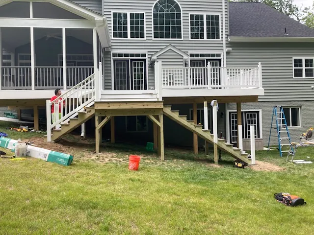 Second-story deck with white railings and stairs beside a screened porch